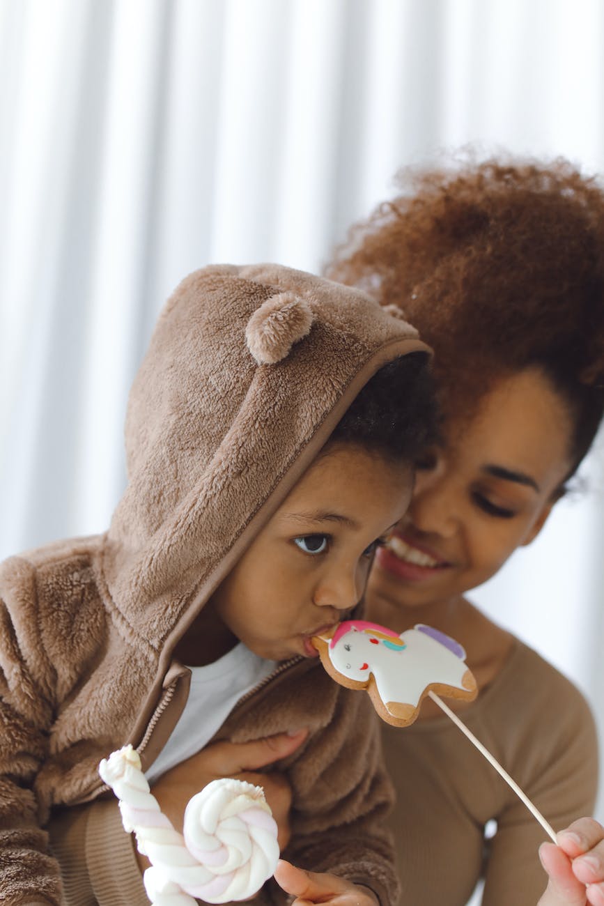 woman holding a boy eating a candy cookie on stick